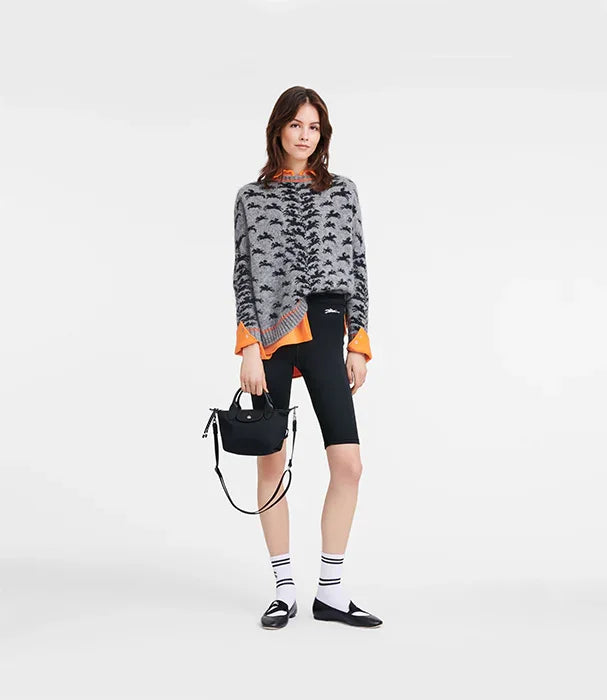 דוגמנית לובשת סוודר אפור עם דוגמה, חולצה כתומה, מכנסי אופניים שחורים ותיק שחור, אופנת CHOZEN