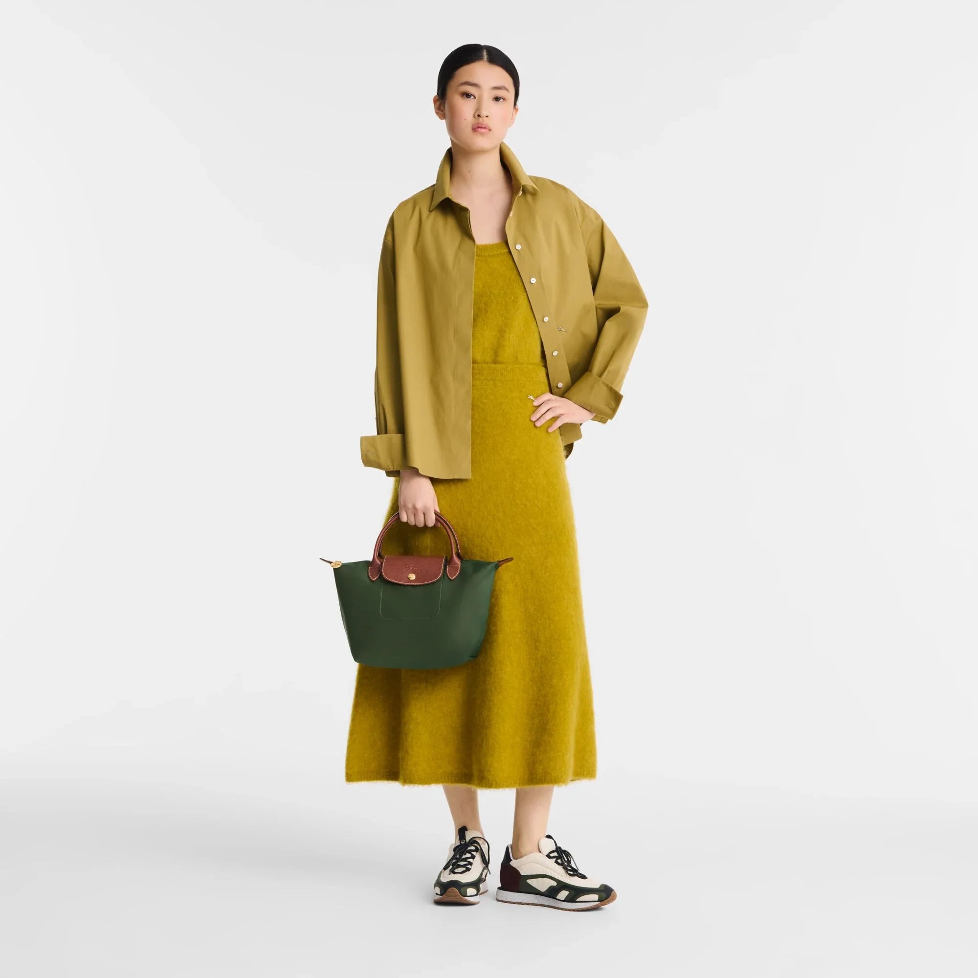 אישה עם שמלה בצבע חרדל וז'קט תואם, מחזיקה תיק ירוק, אופנה CHOZEN מהמותגים המובילים