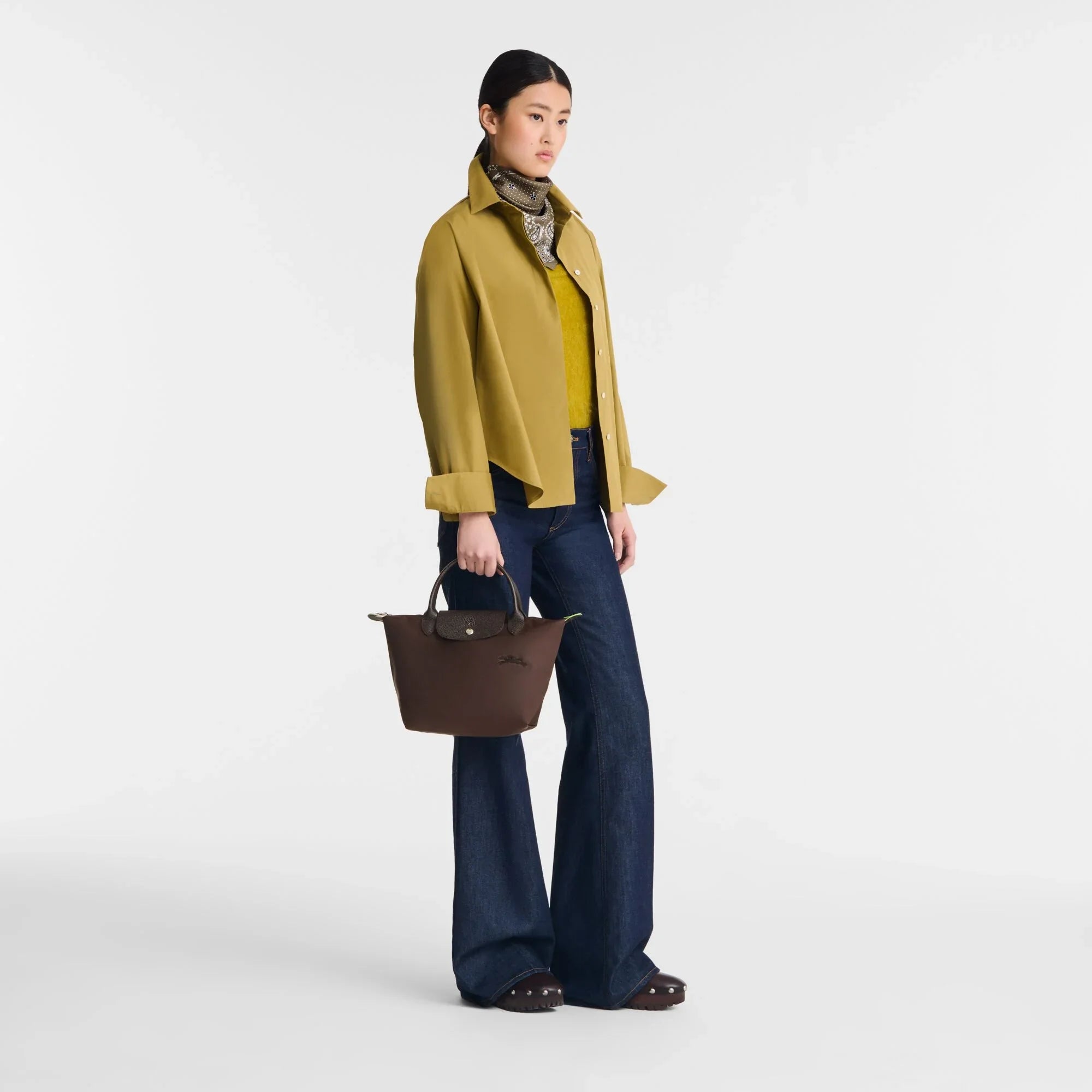 אישה עם תיק חום אופנתי, לובשת חולצה זית ומכנסי ג'ינס, מבית מותג CHOZEN