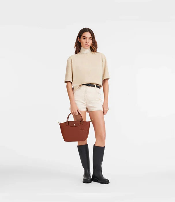 אישה עם חולצה בז', מכנסיים קצרים, מגפי גומי שחורים ותיק חום, אופנה CHOZEN