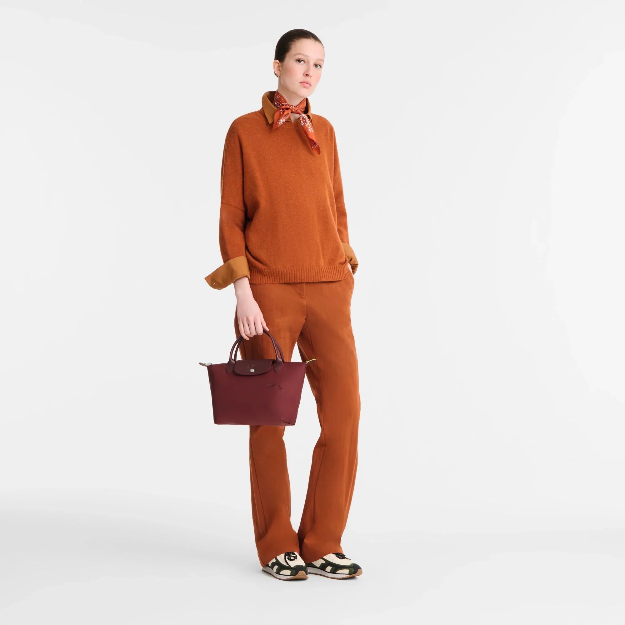 אישה עם חולצה ומכנסיים בצבע חום, צעיף אדום, תיק בורדו ונעלי אופנה, על רקע לבן, CHOZEN