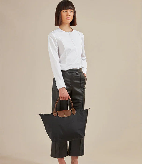 אישה לובשת חולצה לבנה ומכנסי עור מחזיקה תיק שחור אופנתי, צילום סטודיו למותגים בינלאומיים
