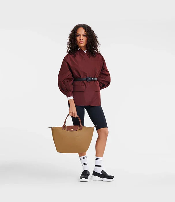 דוגמנית עם ז'קט בורדו, תיק חום, שורטס שחור ונעלי סניקרס בסטייל CHOZEN