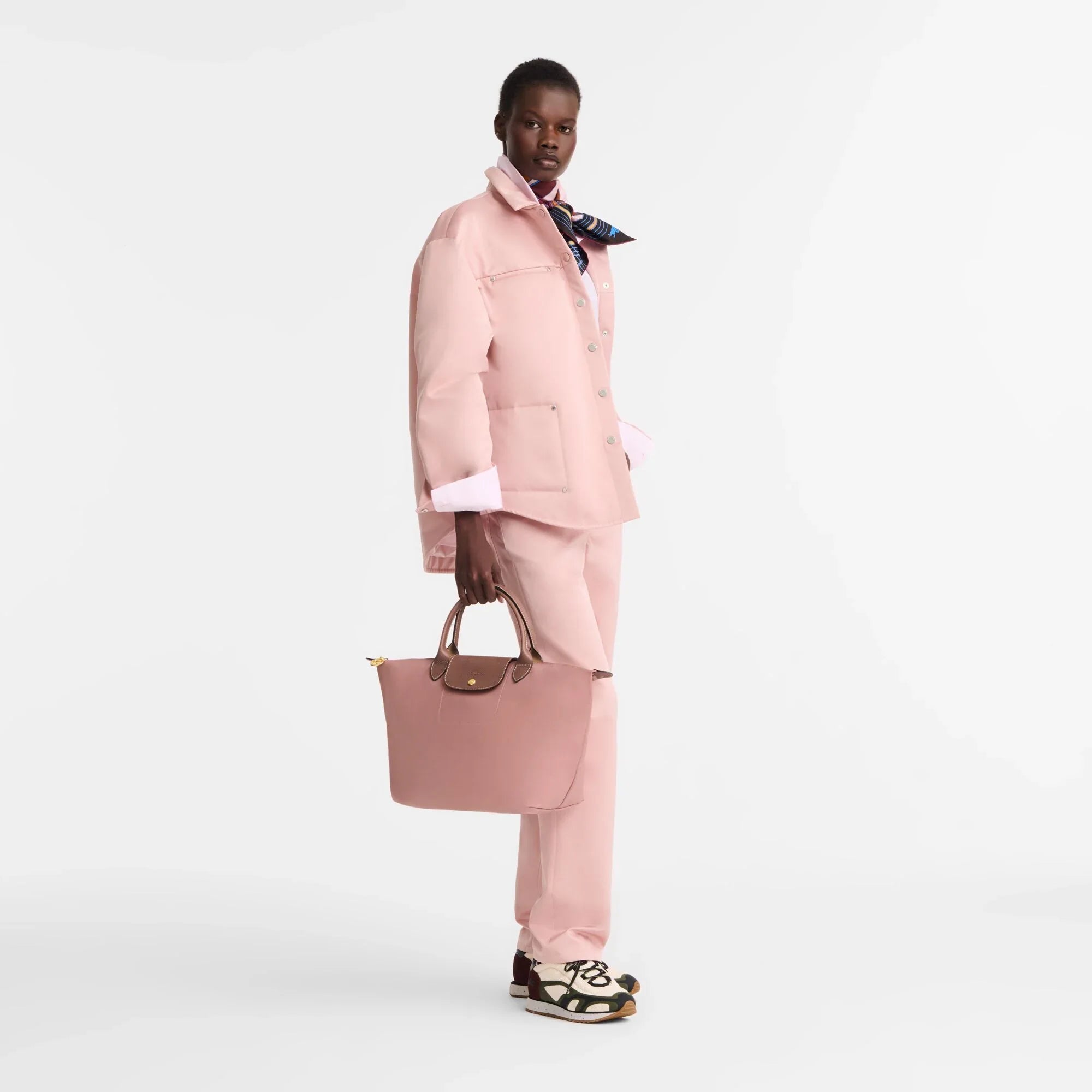 אישה בלבוש ורוד אלגנטי, מחזיקה תיק ורוד, דוגמנית אופנה של מותג CHOZEN