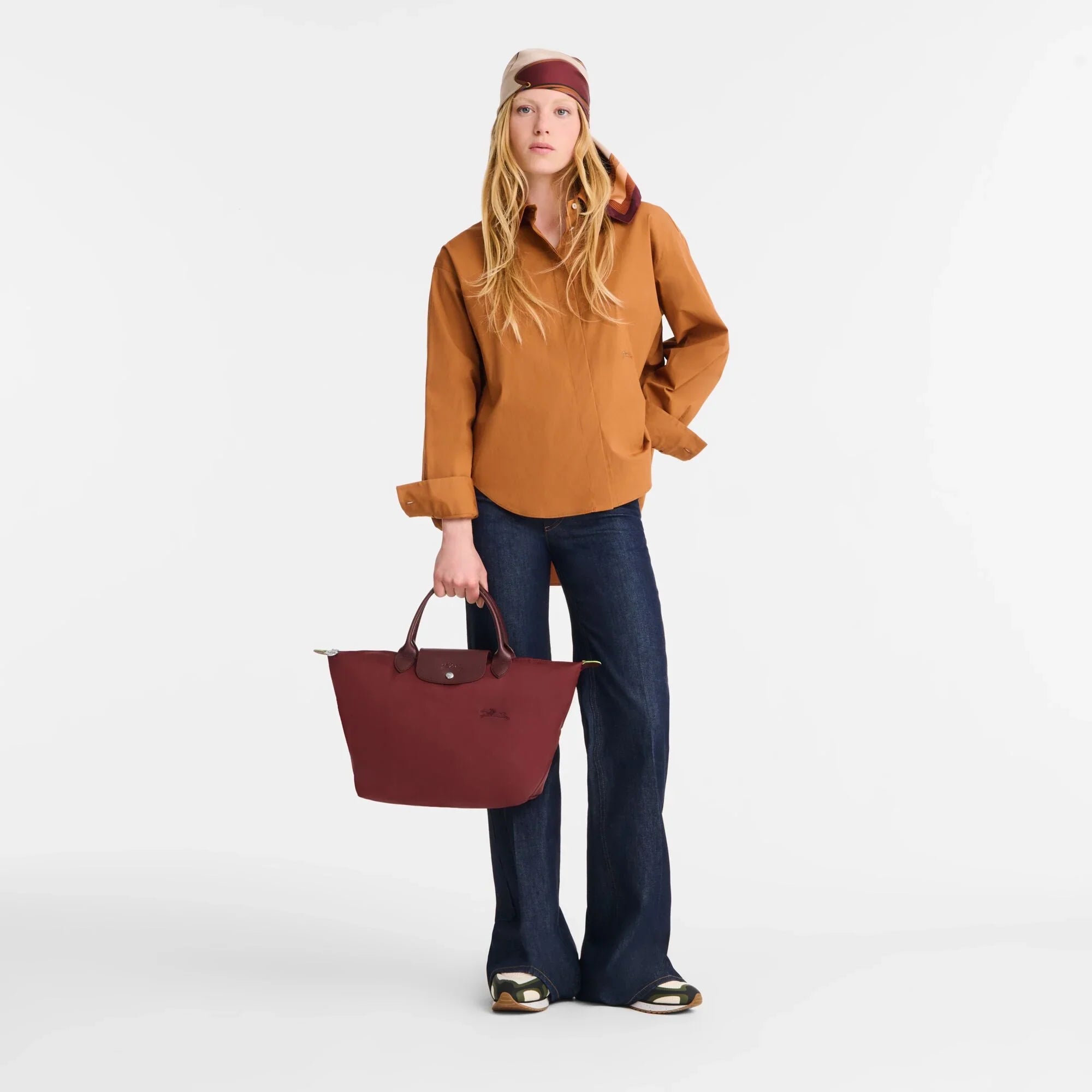 דוגמנית לובשת חולצה חומה, ג'ינס כהה ונושאת תיק בורדו, אופנה יוקרתית CHOZEN