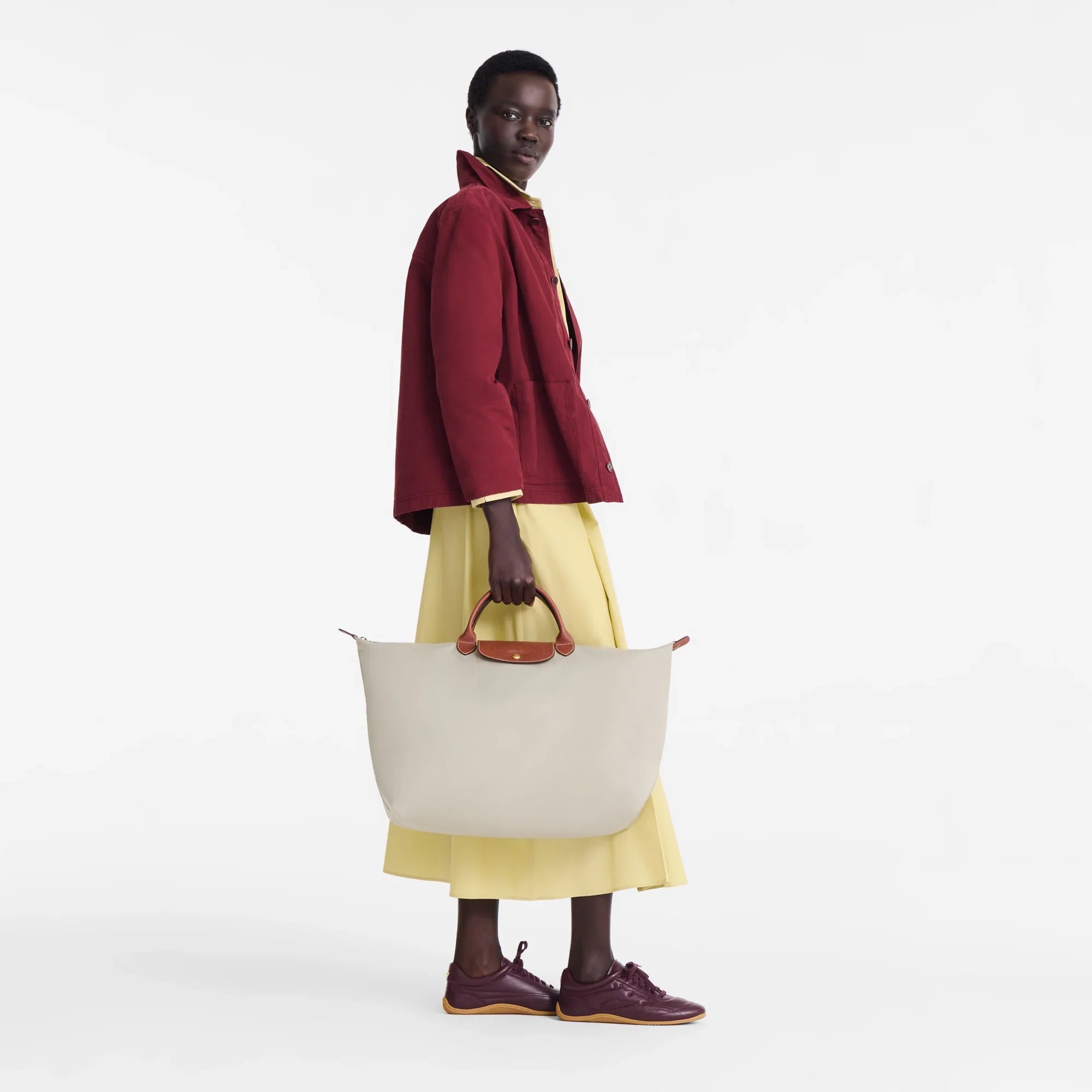 אישה בסטייל לובשת מעיל אדום עם שמלה צהובה, מחזיקה תיק אופנה גדול, מותגים מובילים CHOZEN