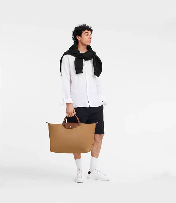 דוגמן לובש חולצה לבנה, מכנסיים קצרים שחורים ונושא תיק חום אופנתי מבית CHOZEN