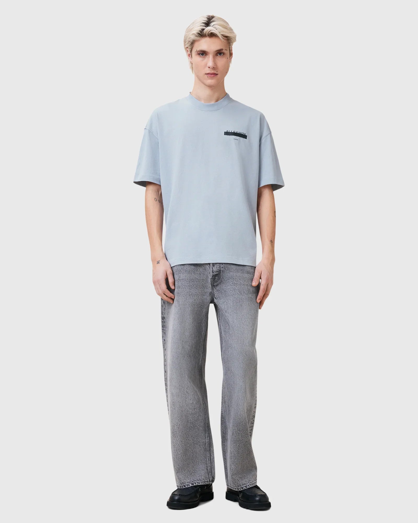 גבר לובש חולצת טי בהירה ומכנסי ג'ינס אפורים עמידה מול רקע לבן, CHOZEN בגדי אופנה לגבר