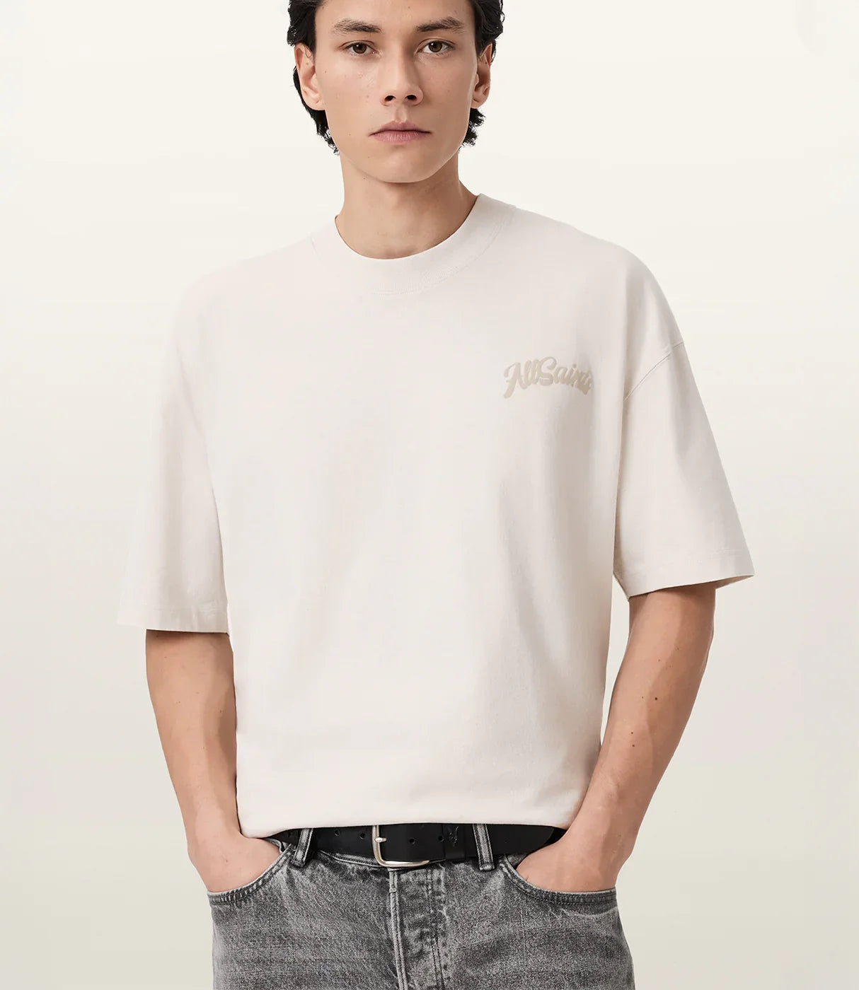 גבר לובש טי שירט לבנה עם הדפס קטן, שרוולים קצרים, ג'ינס אפור וחגורה שחורה