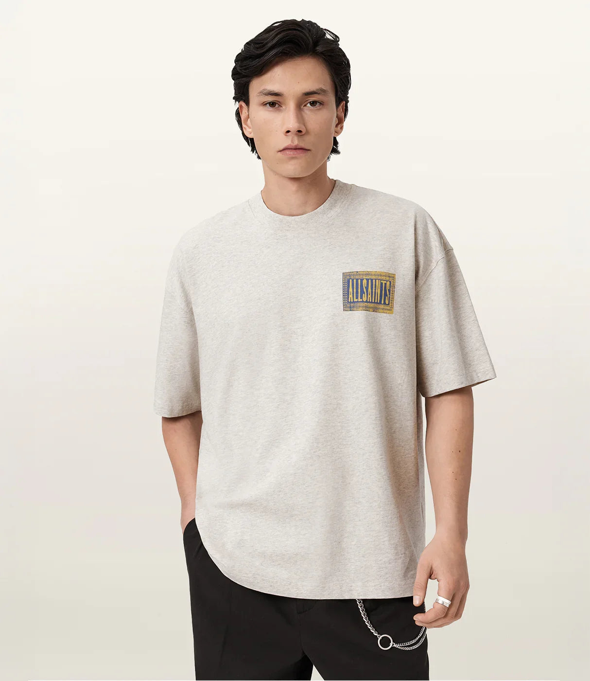 גבר לובש חולצת טי שירט אפורה עם כיתוב ALLSAINTS, שרשרת לחגורה, סטייל אופנתי