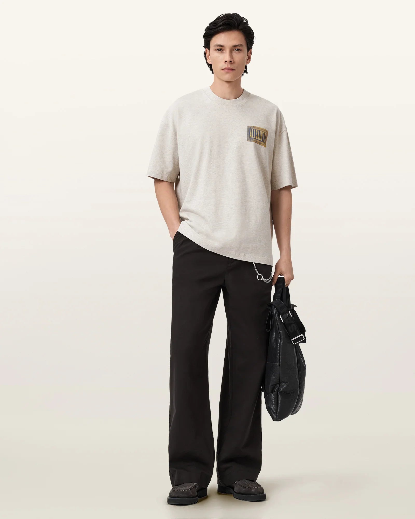 גבר עם חולצה בהירה עם הדפס, מכנסיים כהים ותיק שחור, אופנה עדכנית לגברים