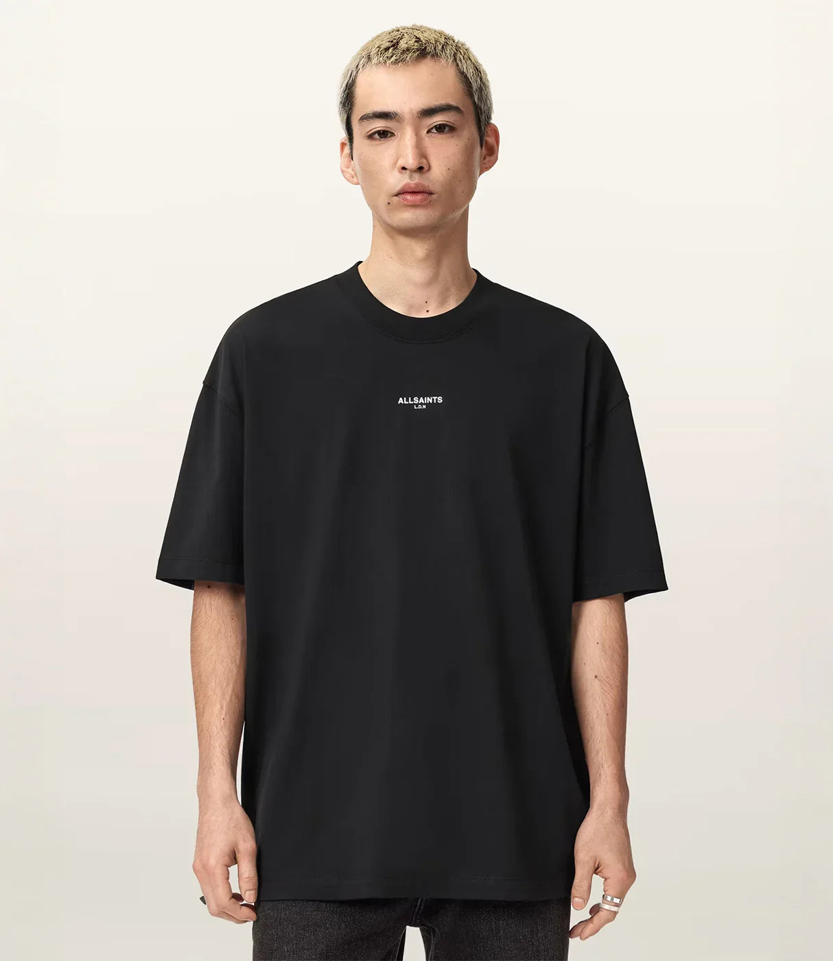 גבר עם שיער קצר לובש חולצת טי שחורה עם כיתוב ALLSAINTS במרכז החזה על רקע בהיר
