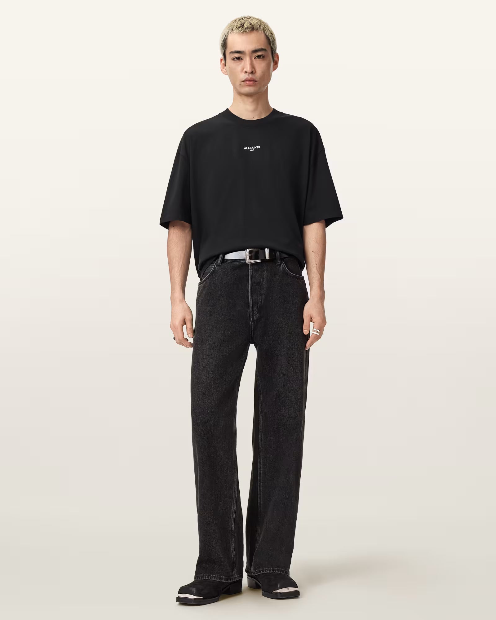 גבר לובש חולצת טי שחורה עם כיתוב לבן ומכנסי ג'ינס שחורים בגזרה רחבה, אופנת רחוב עדכנית