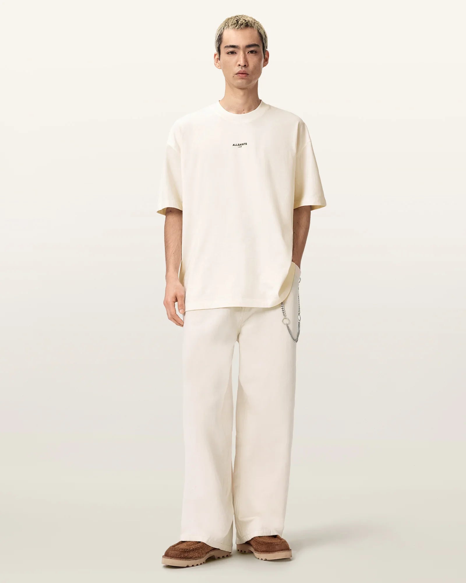 דוגמן לובש טי שירט בהירה עם כיתוב ומכנסיים בגזרה רחבה בצבע שמנת, נעלי בית חומות