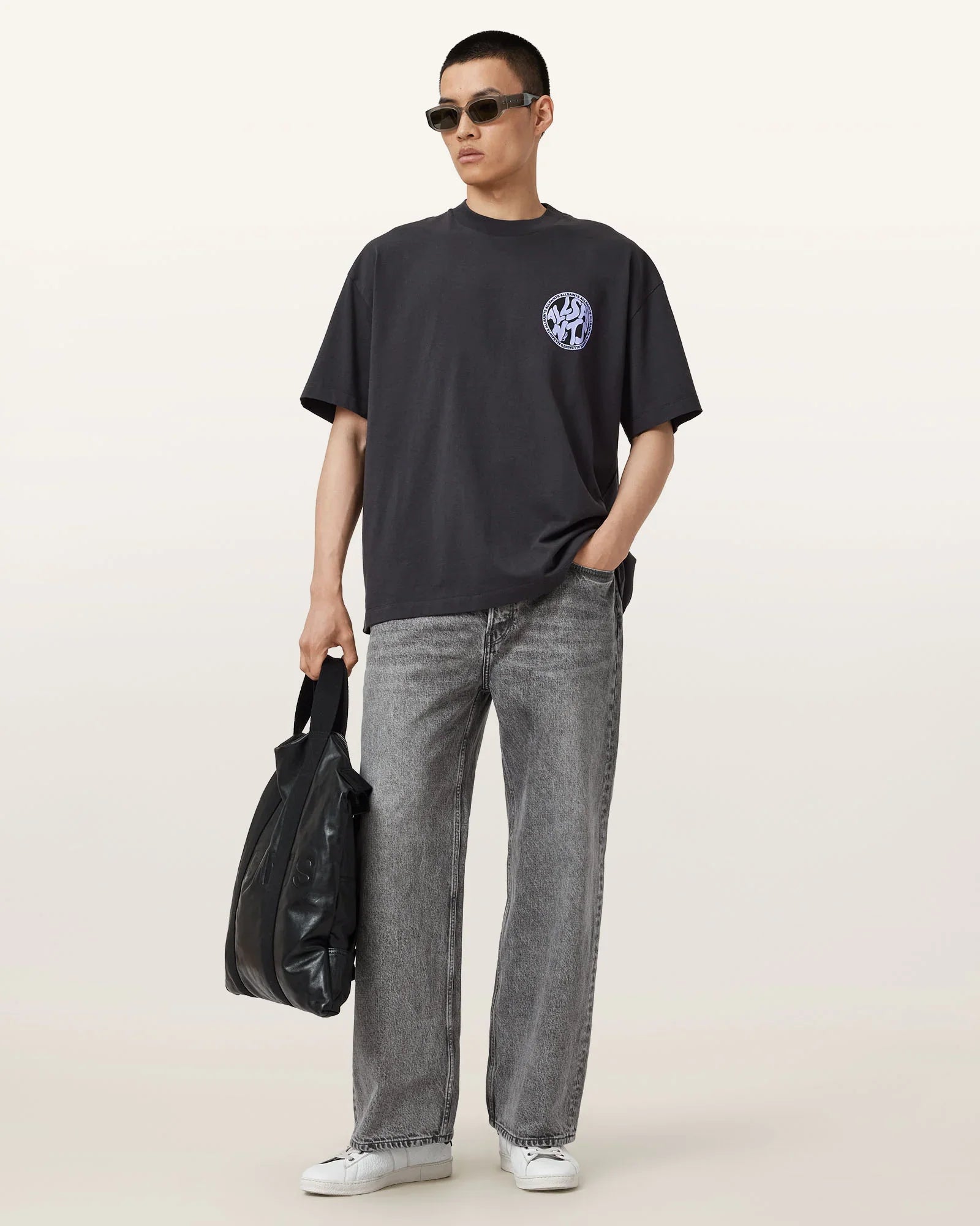 גבר עם חולצת טי כהה, ג'ינס אפור, משקפי שמש ותיק שחור, אופנה מודרנית CHOZEN