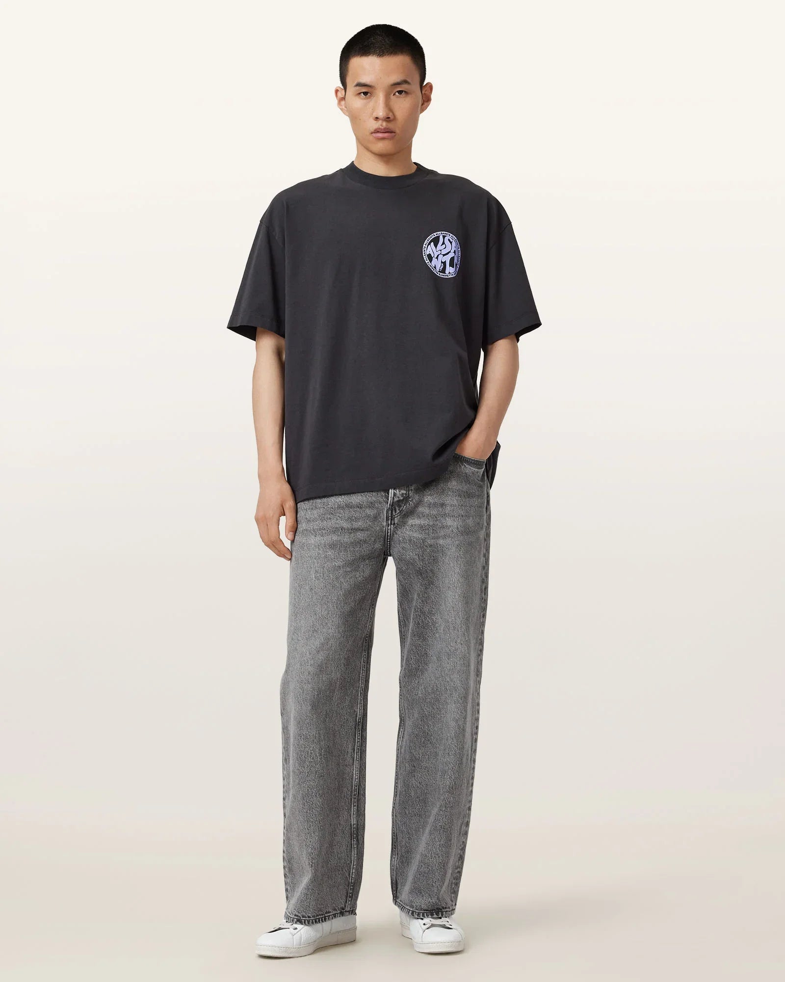 דגם לובש חולצת טי שחורה עם הדפס קטן וחזית, ג'ינס אפור ונעלי סניקרס, מבית CHOZEN