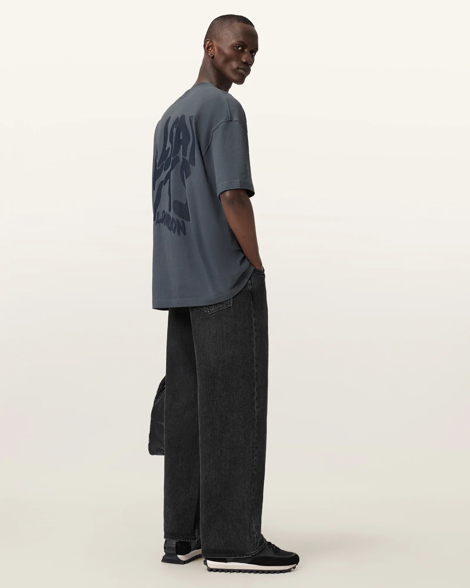 גבר עם חולצת טי אפורה עם הדפס גרפי, מכנסי ג'ינס שחורים ונעלי סניקרס, אופנה CHOZEN