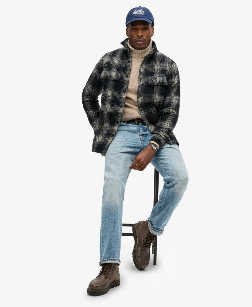 גבר לובש חולצה משובצת, ג׳ינס כחול, סוודר בז׳ וכובע כחול, אופנה לגבר מבית CHOZEN