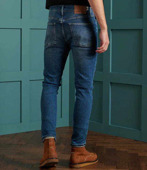 ג'ינס סקיני לגבר בצבע כחול, נעליים חומות, רקע חדר מודרני, CHOZEN מותגים מובילים