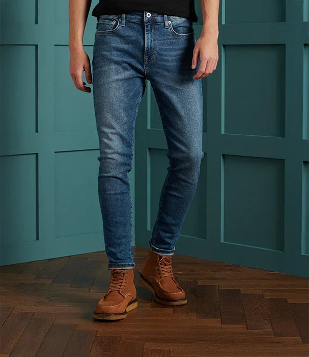 גבר לובש ג'ינס כחול ונעלי עור חומות, רקע קיר ורצפת עץ, CHOZEN, מותגים מובילים