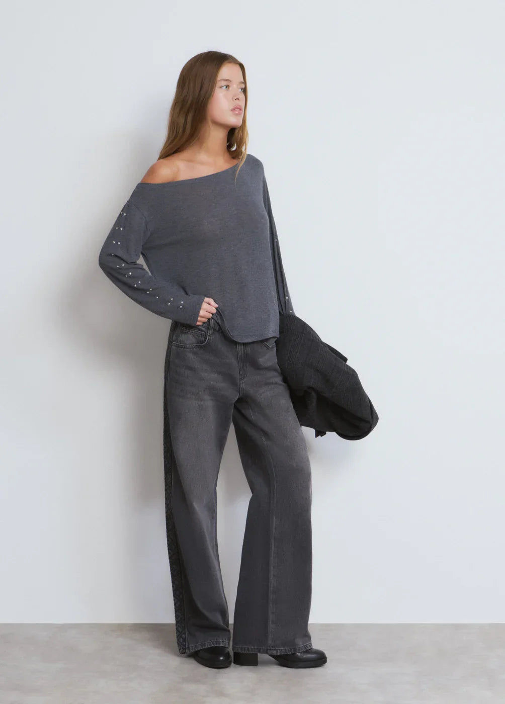 אישה בלבוש אופנתי של חולצה אפורה עם כתף חשופה ומכנסי ג'ינס כהים רחבים, CHOZEN אופנה