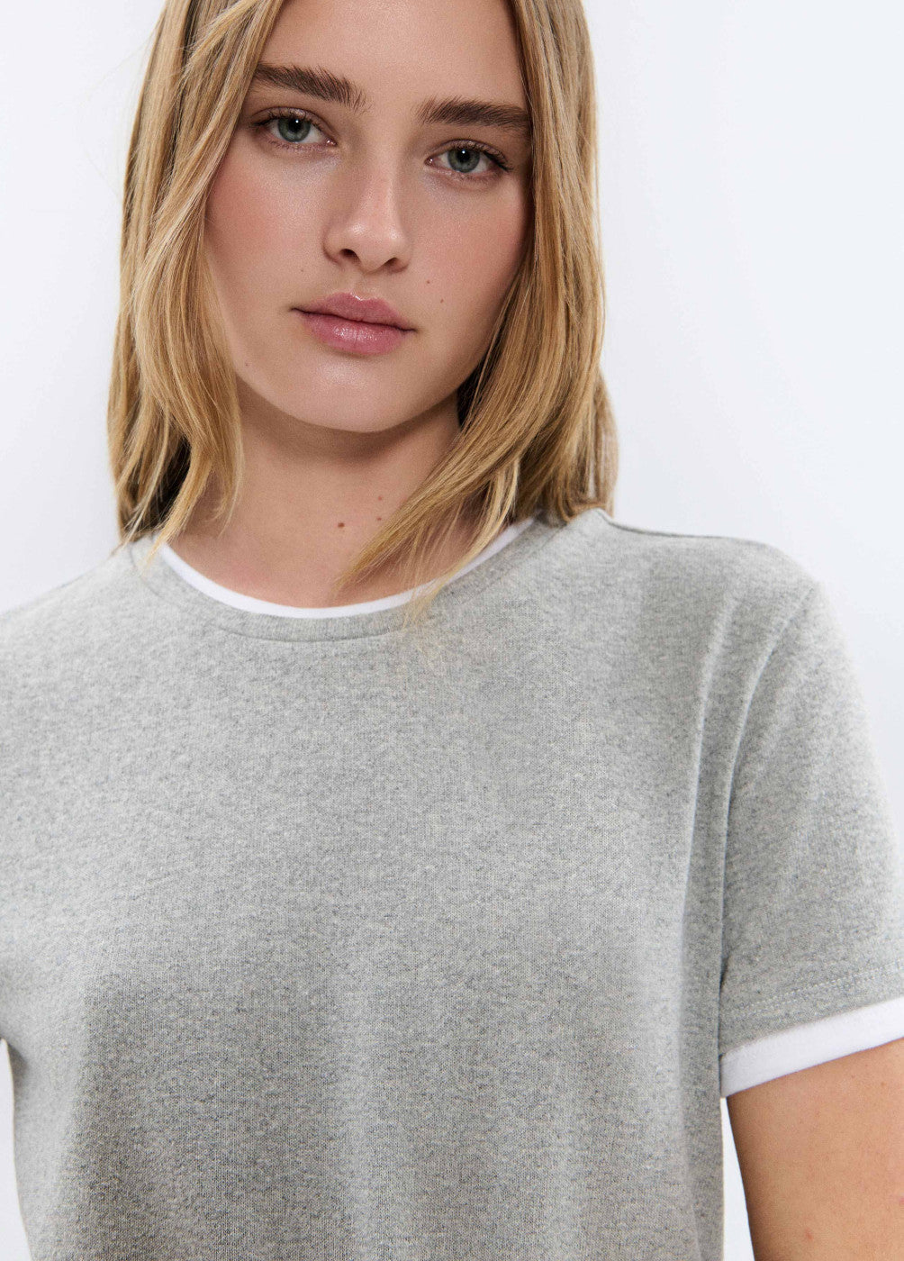 אישה לובשת טי שרט אפורה קצרה עם שולי שרוולים ולולאה לבנה, צילום תקריב אופנה