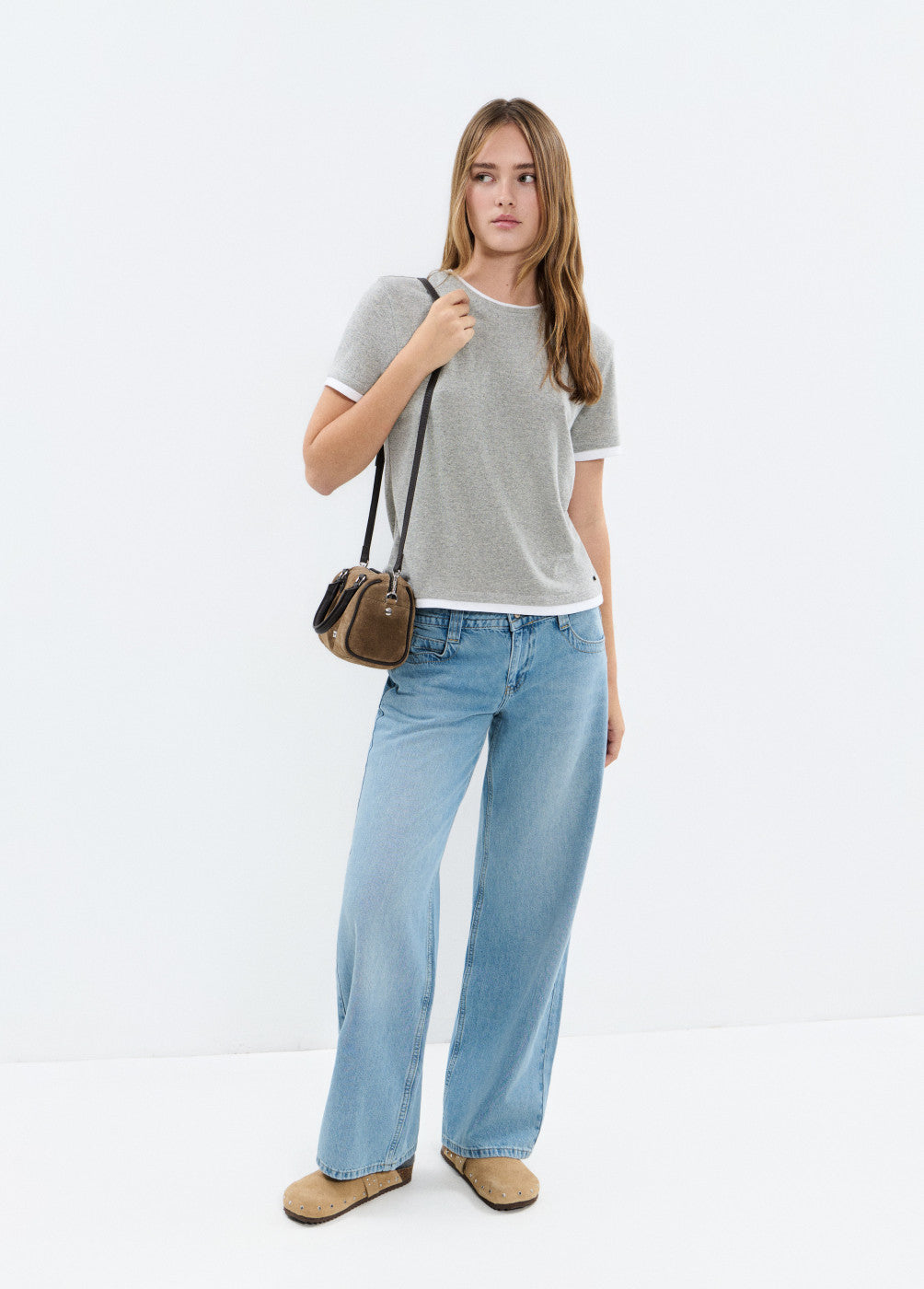 אישה לובשת חולצה אפורה קצרה, ג'ינס רחב, נעלי מוקסין ותיק קטן, מראה יום יומי אופנתי