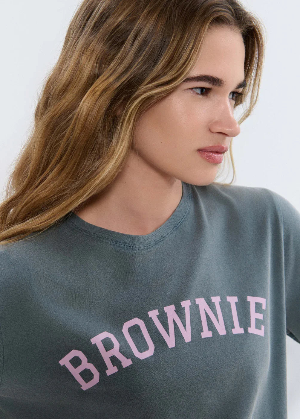 אישה לובשת חולצת טריקו אפורה עם כיתוב ורוד BROWNIE, אופנה קז'ואל לנשים