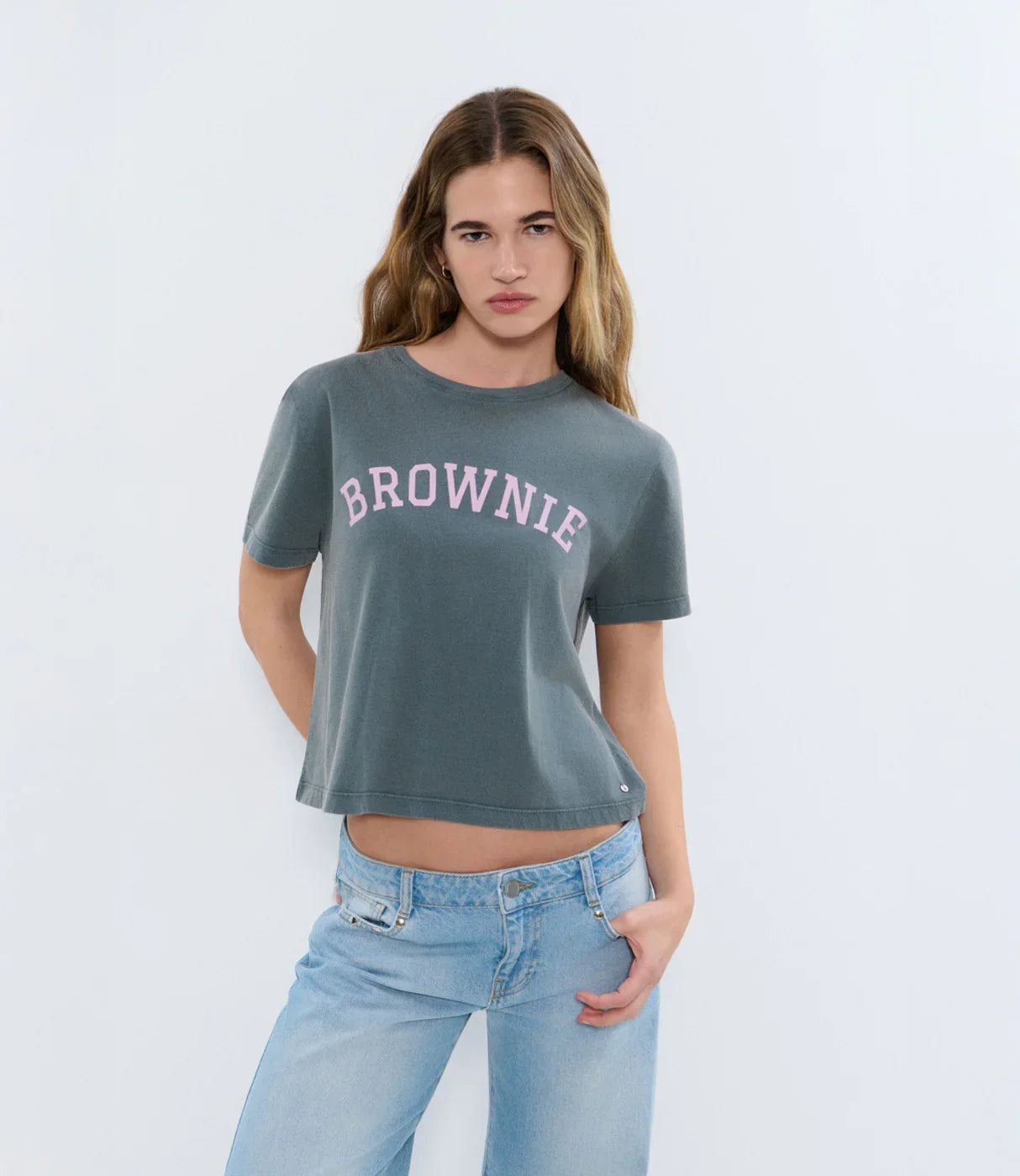 אישה עם שיער ארוך לובשת חולצת טי אפורה עם הכיתוב BROWNIE ומכנסי ג'ינס כחולים