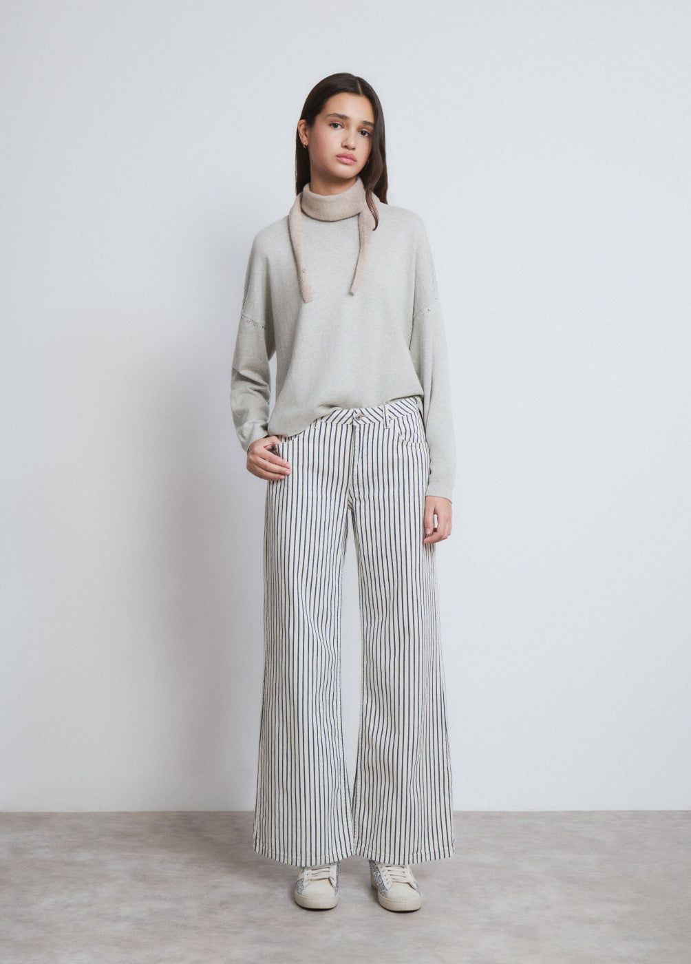 דוגמנית לובשת סוודר אפור מכופתר ומכנסי פסים רחבים, אופנה נשית מודרנית