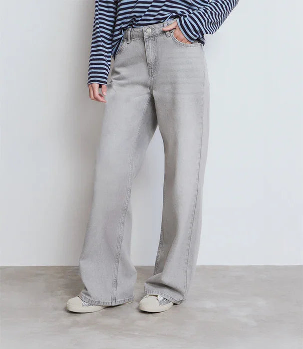 ג'ינס רחב אפור לנשים מבית CHOZEN, חולצת פסים כחולה ונעלי סניקרס, מצולם על רקע קיר לבן