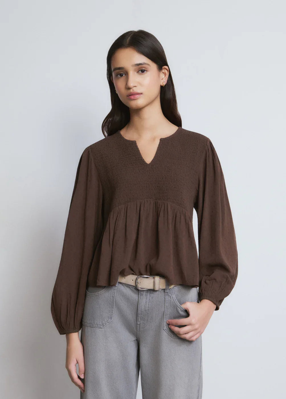 דוגמנית לובשת חולצה חומה עם שרוולים ארוכים, מכנסיים אפורים ובלייז CHOZEN