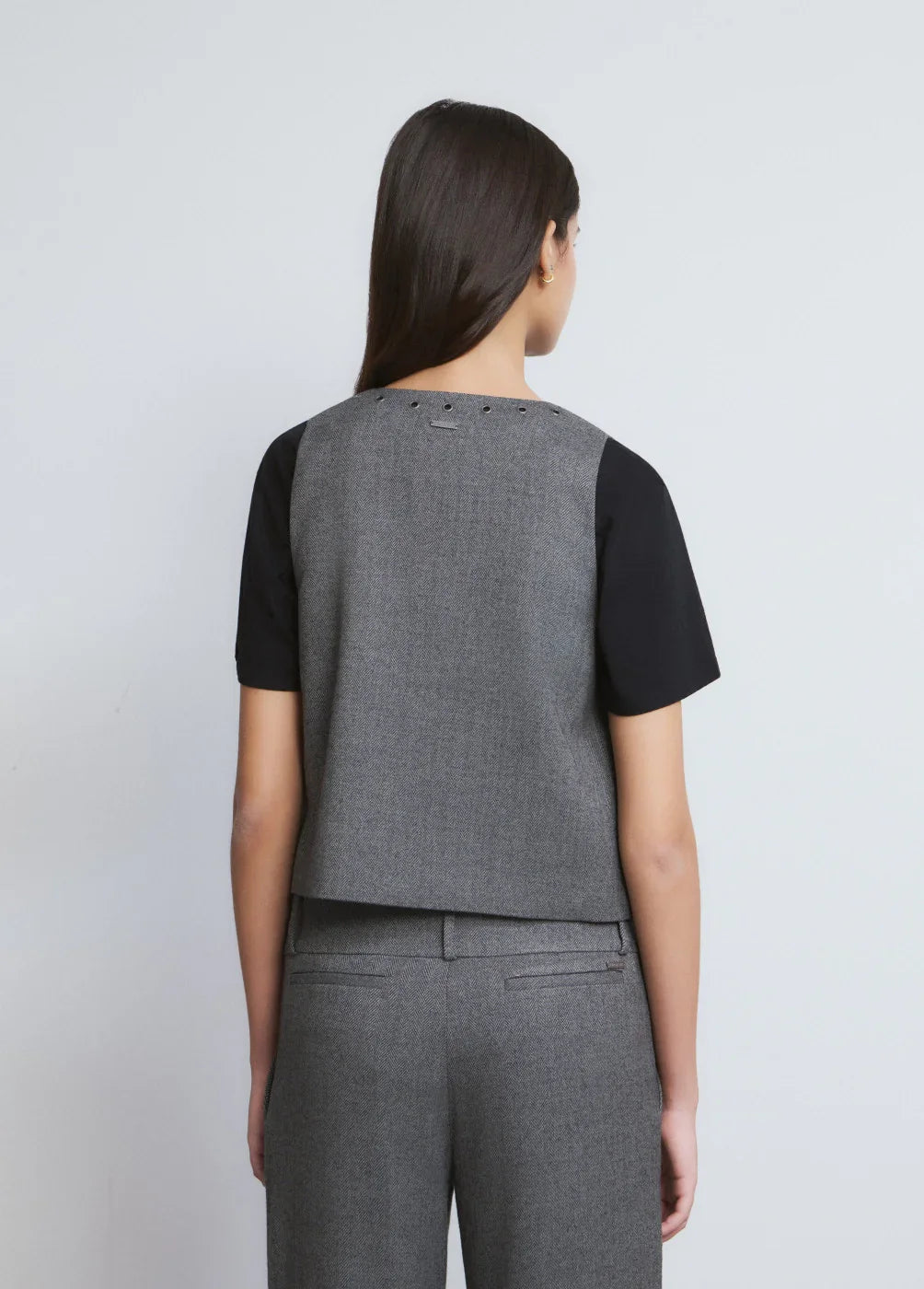 אישה לובשת חליפת מכנסיים מחויטת אפורה עם חולצת טי שחורה, צילום מגב על רקע ניטרלי