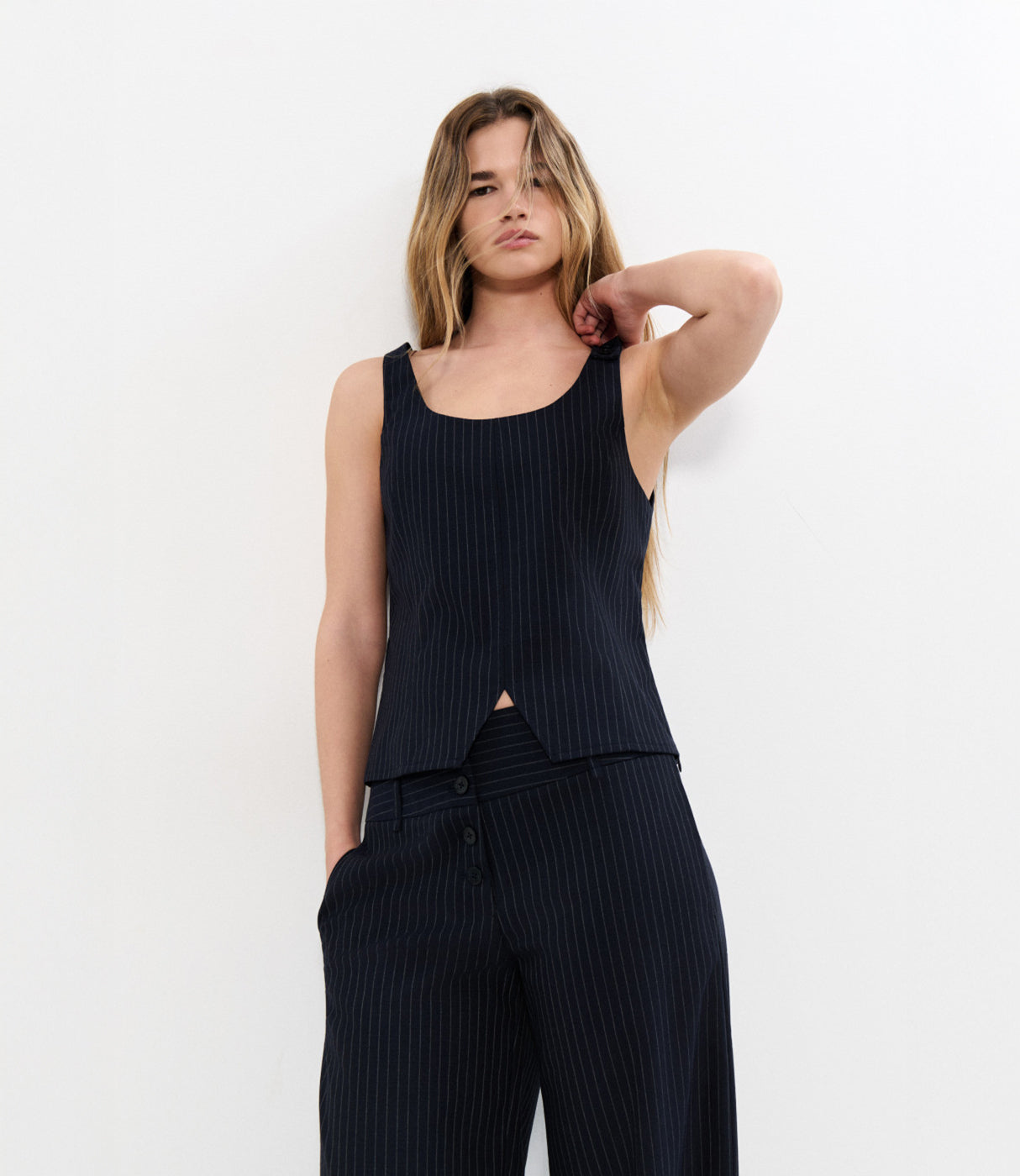 אישה לובשת סט חליפה פסים שחור ללא שרוולים, חזית מינימליסטית, רקע לבן