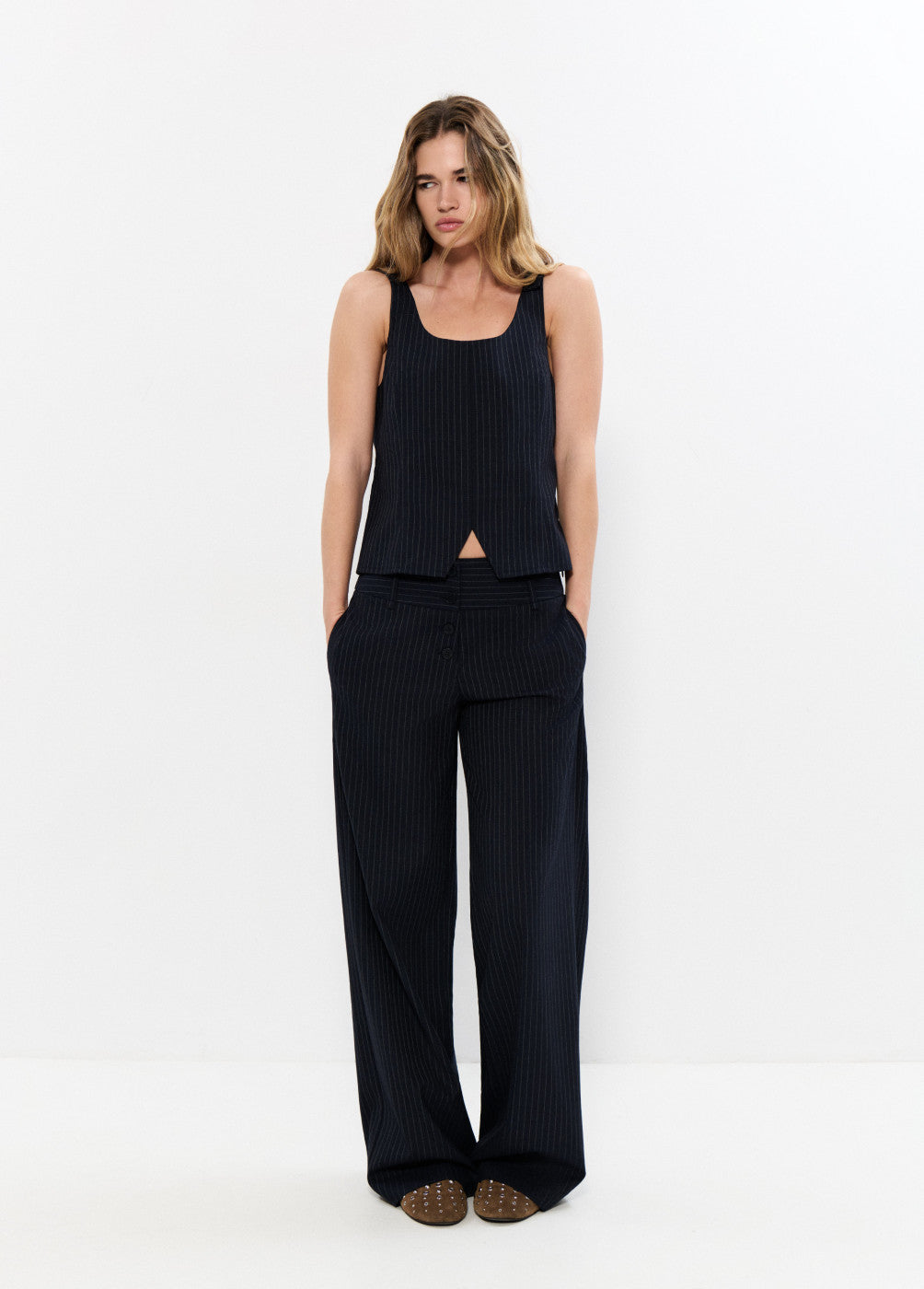 אישה עם חולצת גופיה ומכנסיים מחויטים מפוספסים בצבע שחור, לוק קז'ואל אלגנטי לאופנת נשים