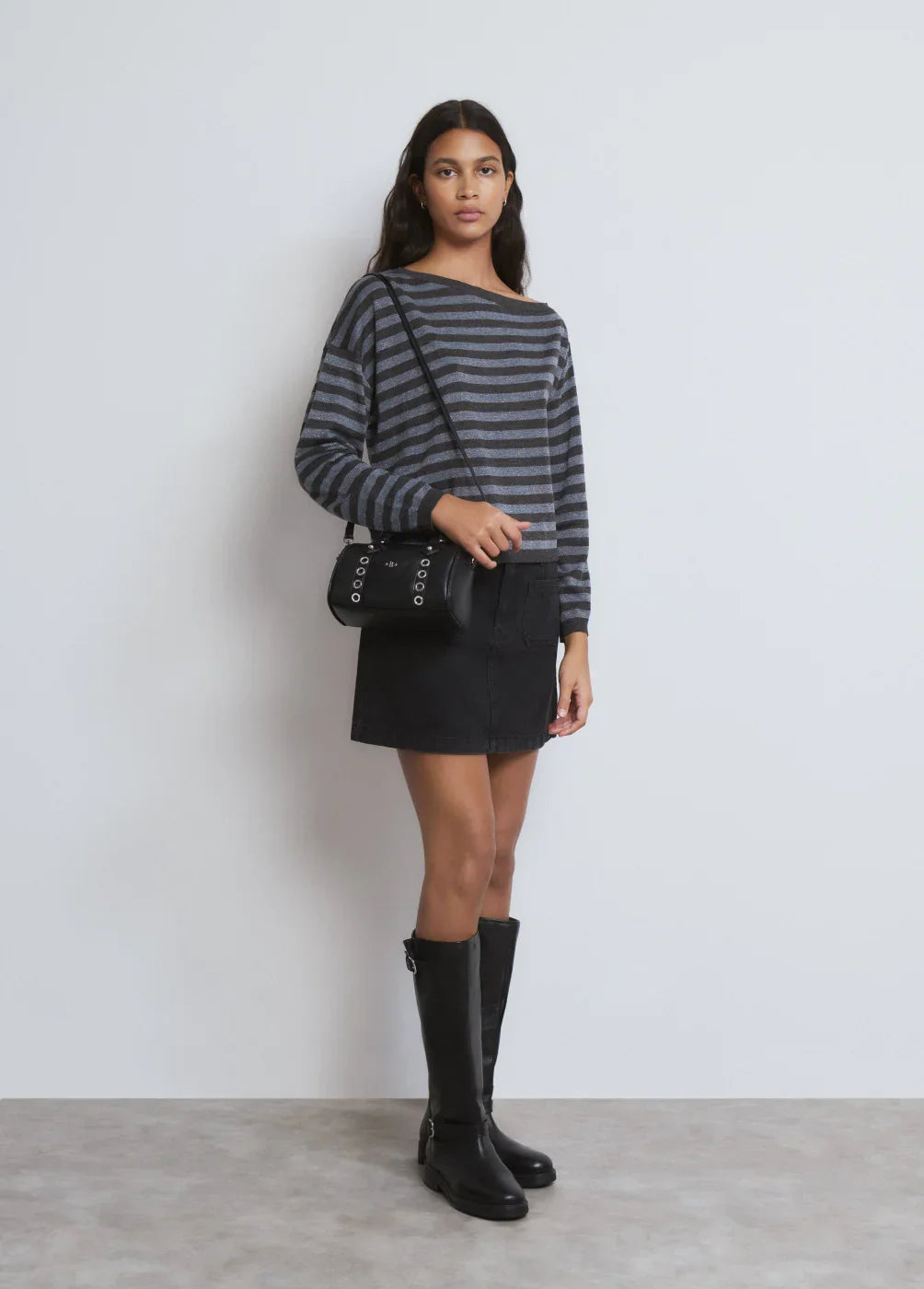 אישה לובשת חולצת פסים אפורה, חצאית שחורה, תיק צד ומגפיים שחורים ממותגי CHOZEN