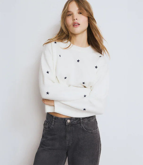 דוגמנית לובשת סוודר לבן עם כוכבים שחורים ומכנסי ג'ינס כהים, אופנה CHOZEN