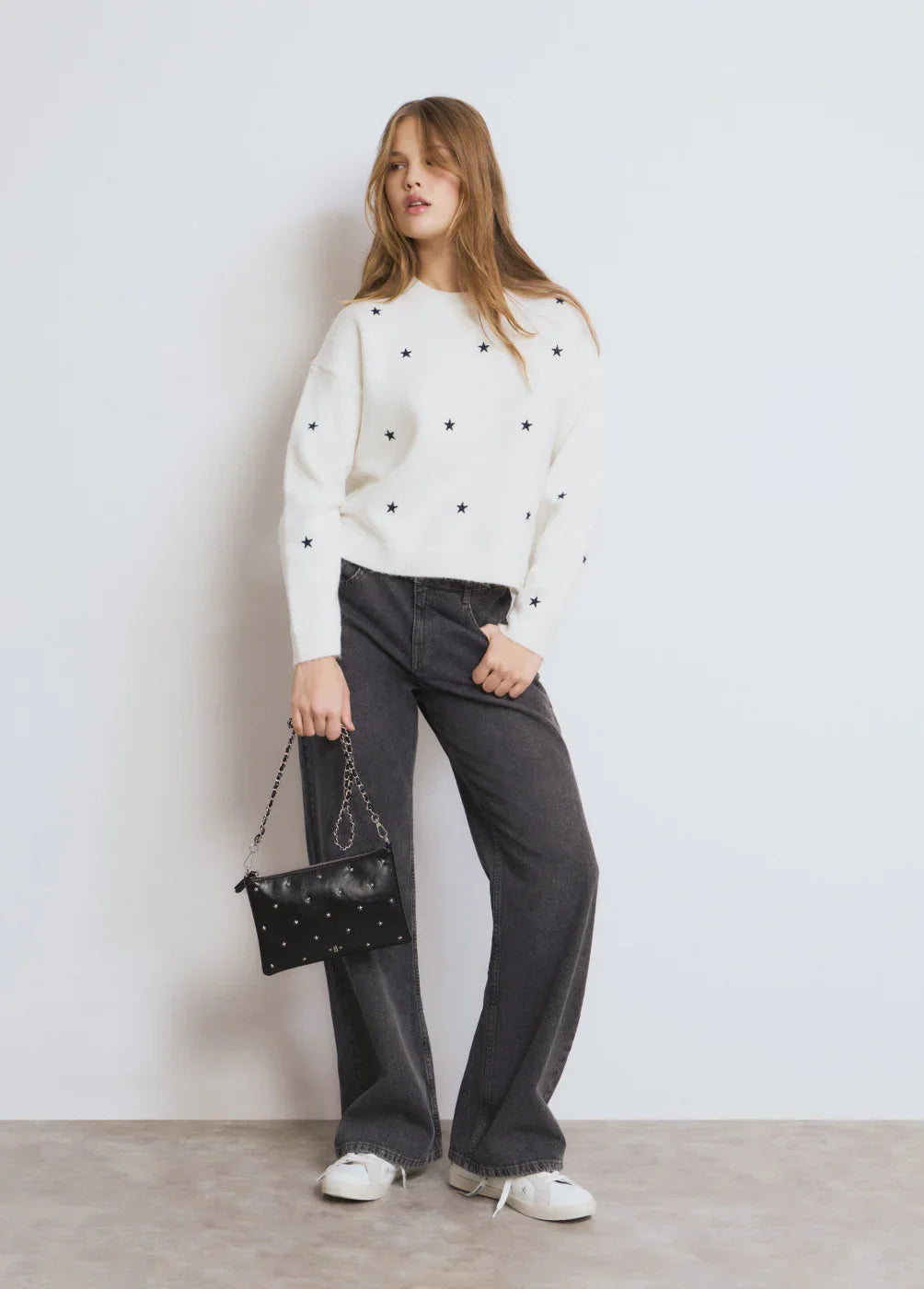 דוגמנית בלבוש טרנדי של CHOZEN, סווטשירט לבן עם כוכבים, ג'ינס כהה ותיק שחור מעוצב