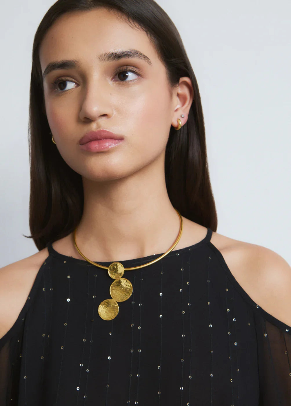 אישה עם שמלת ערב שחורה ושרשרת זהב עם תליון עגול, עגילי זהב עדינים