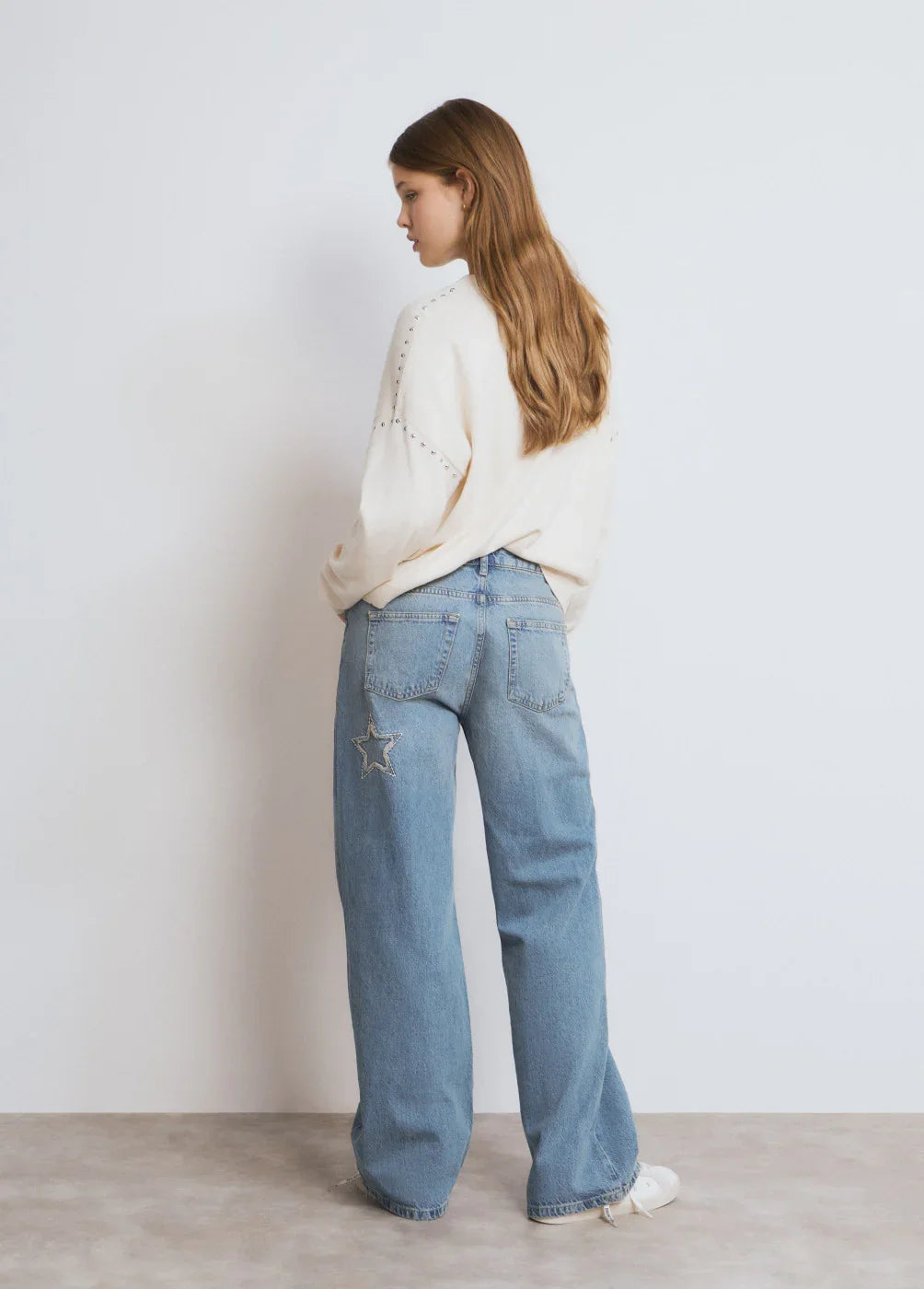 דוגמנית לובשת ג'ינס כחול רחב עם כוכב בכיס אחורי וסוודר שמנת, CHOZEN אופנה מובילה