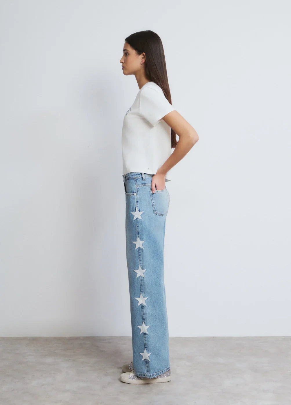 דוגמנית לובשת ג'ינס כחול בהיר עם כוכבים לבנים בצד, חולצה לבנה, רקע לבן, אופנה CHOZEN