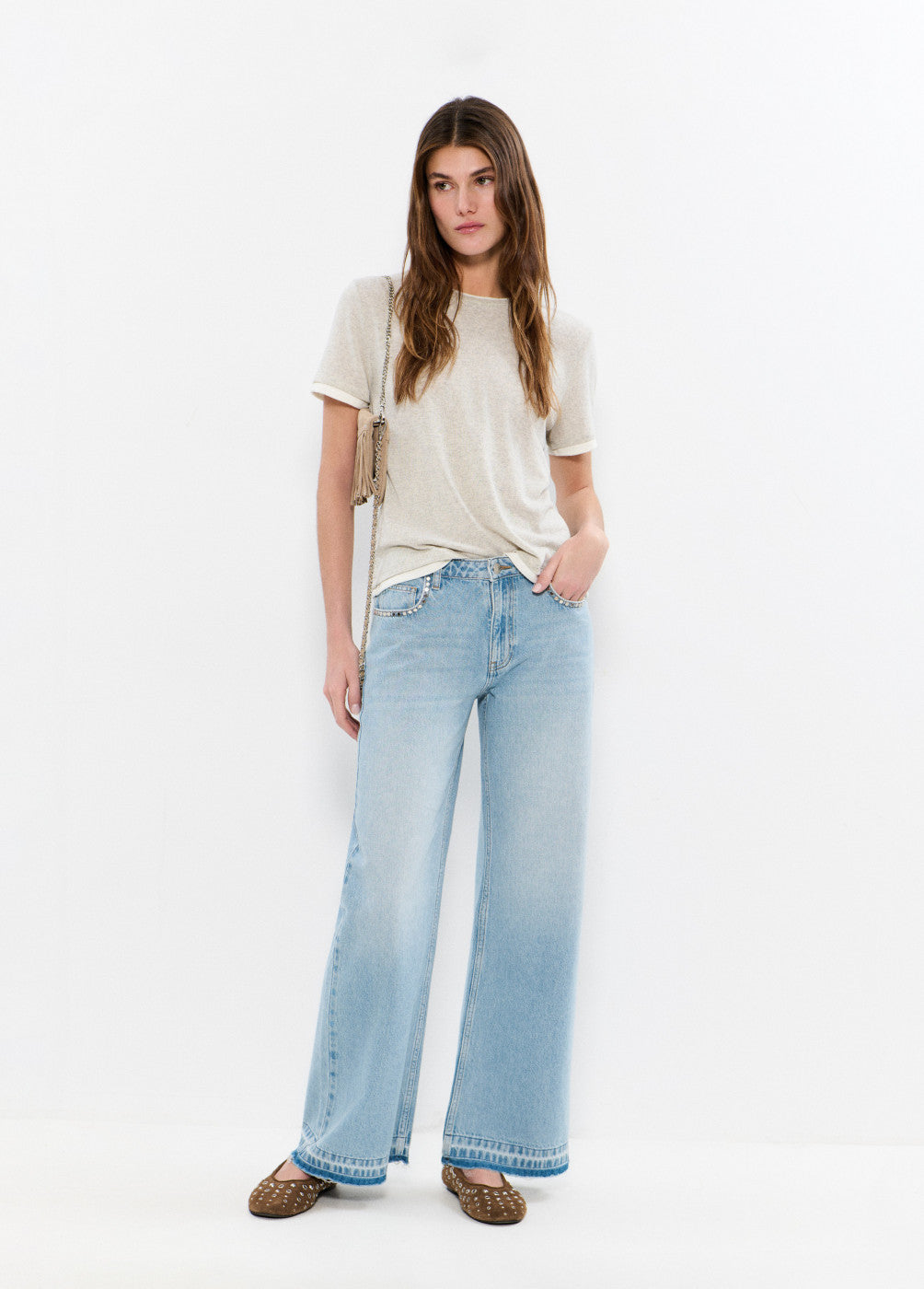 אישה עם ג'ינס רחב בגזרה גבוהה, חולצה בהירה ותיק צד, רקע לבן מינימליסטי