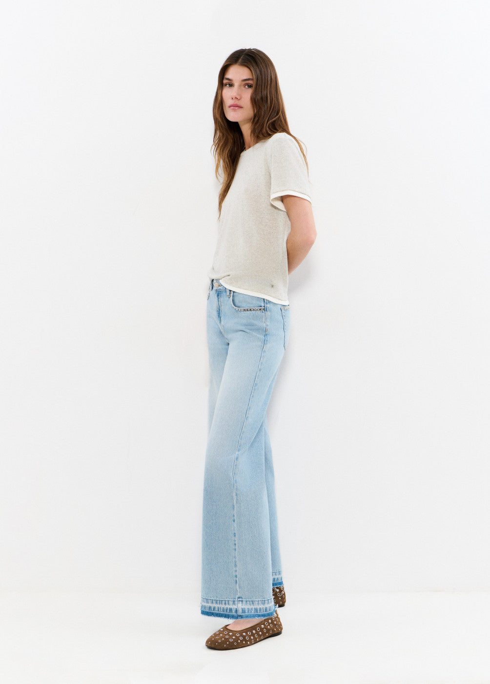 אישה עם חולצה קצרה בצבע בז' ומכנסי ג'ינס בגזרה רחבה, עומדת על רקע לבן