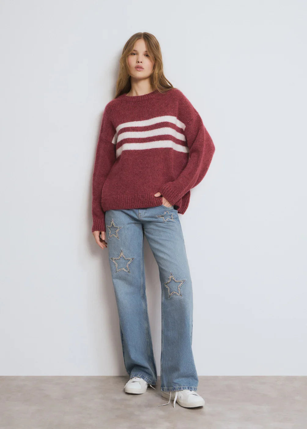 דוגמנית לובשת סוודר בורדו עם פסים לבנים ומכנסי ג'ינס רחבים עם כוכבים, אופנת נשים CHOZEN