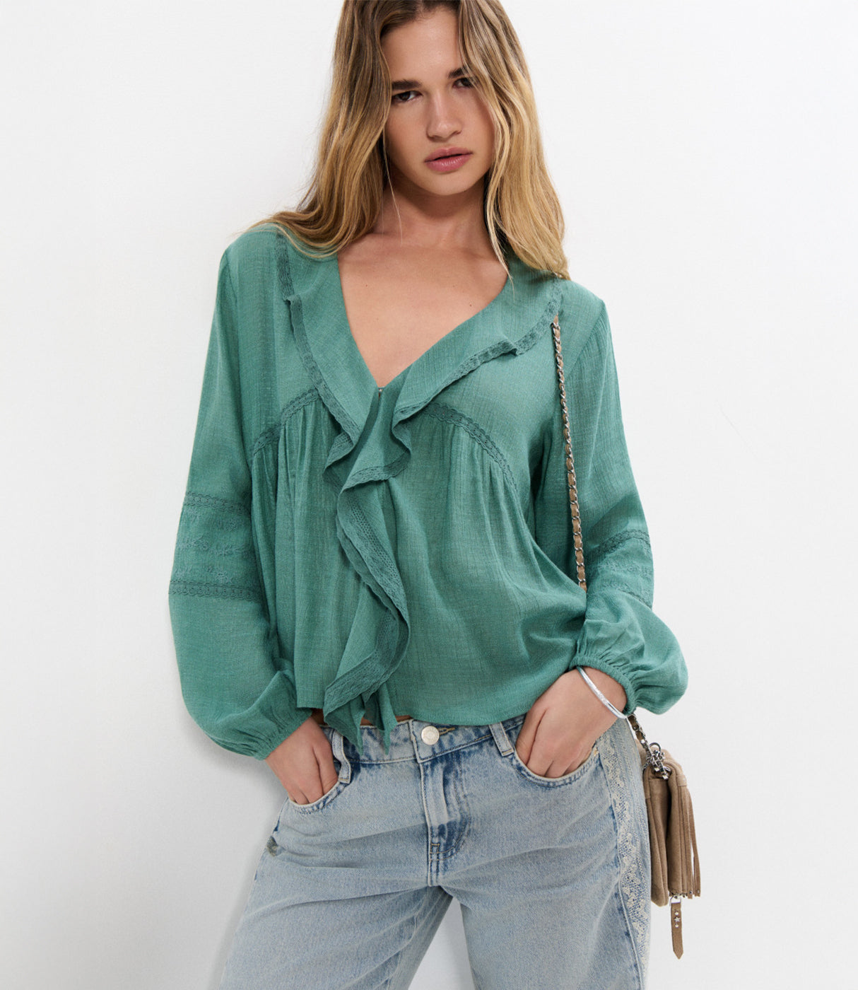 אישה לובשת חולצה ירוקה עם וולנים ומכנסי ג'ינס בהירים, מראה אופנתי קז'ואל