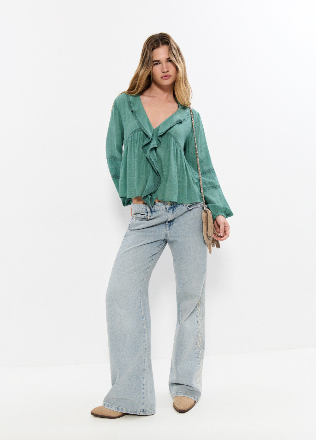 אישה לובשת חולצה ירוקה עם דיטיילים רפויים ומכנסי ג'ינס רחבים אופנתיים