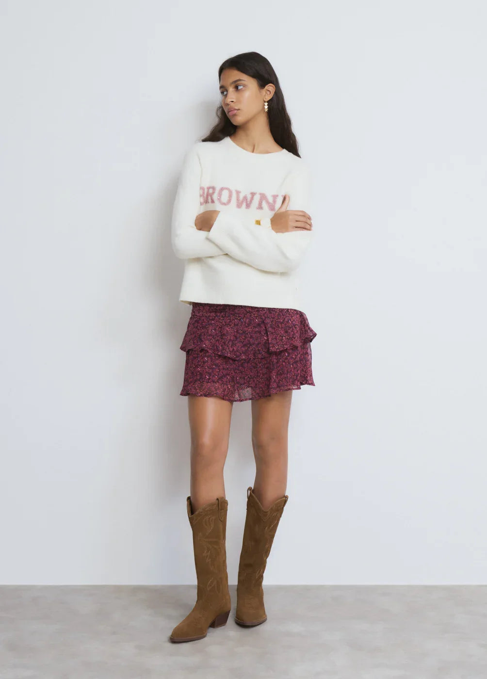 דוגמנית לובשת סוודר לבן עם כיתוב BROWNIE, חצאית פרחונית ורודה ומגפיים חומים, אופנה טרנדית CHOZEN