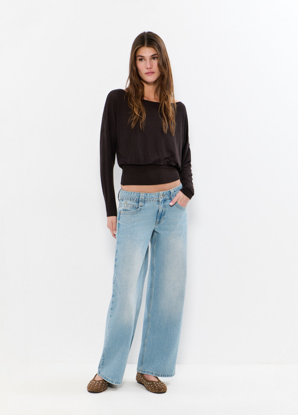 דוגמנית לובשת ג׳ינס כחול בגזרה רחבה וסוודר כהה, אופנת נשים טרנדית