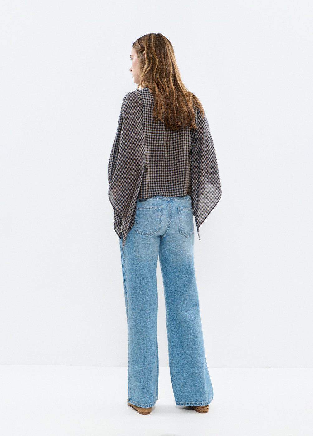 אישה עם חולצה משובצת רחבה ומכנסי ג'ינס בגזרה ישרה, מבט מאחור באולפן לבן