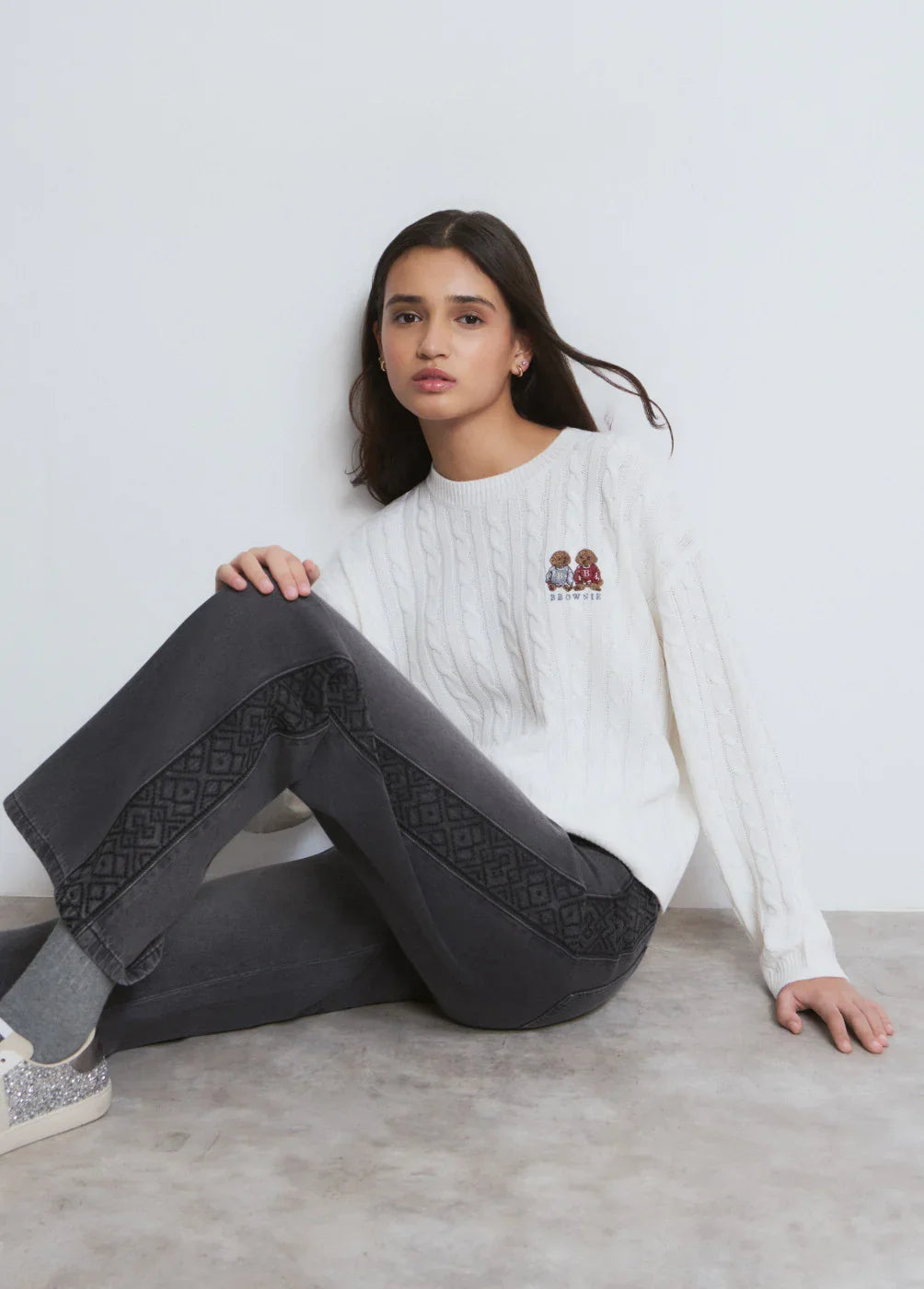 דוגמנית לובשת סוודר לבן סרוג עם רקמה ושם המותג BROWSER, ומכנסי ג'ינס כהים. CHOZEN אופנה יוקרתית.